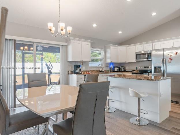 kitchen with hanging light fixtures, appliances with stainless steel finishes, a kitchen island, light hardwood / wood-style floors, and white cabinets