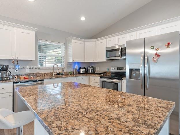 kitchen with a kitchen island, white cabinetry, appliances with stainless steel finishes, and vaulted ceiling