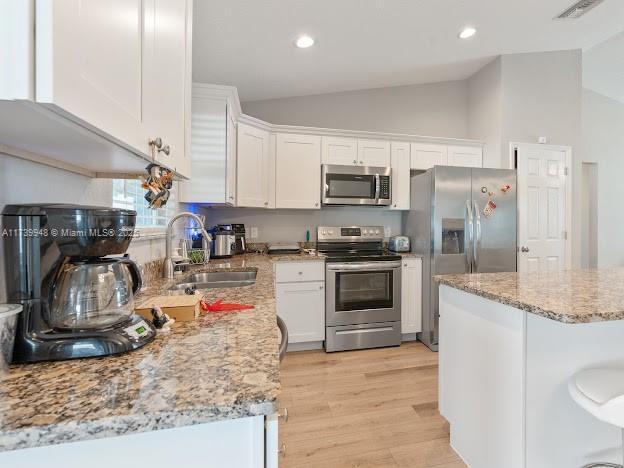 kitchen with vaulted ceiling, appliances with stainless steel finishes, sink, white cabinets, and light wood-type flooring