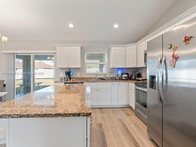 kitchen with stainless steel appliances, white cabinetry, light stone counters, and light wood-type flooring