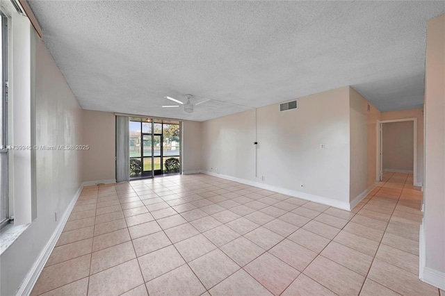 spare room featuring ceiling fan, a wall of windows, a textured ceiling, and light tile patterned floors