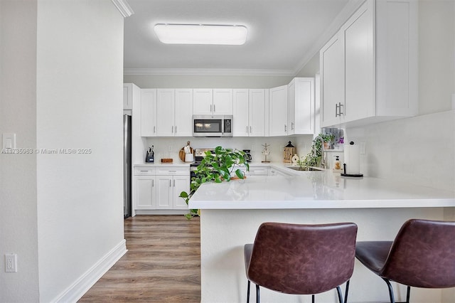 kitchen with white cabinetry, sink, a breakfast bar area, kitchen peninsula, and stainless steel appliances