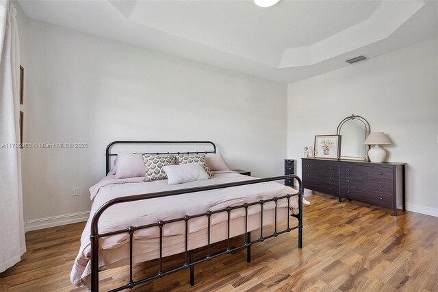 bedroom with hardwood / wood-style floors and a raised ceiling