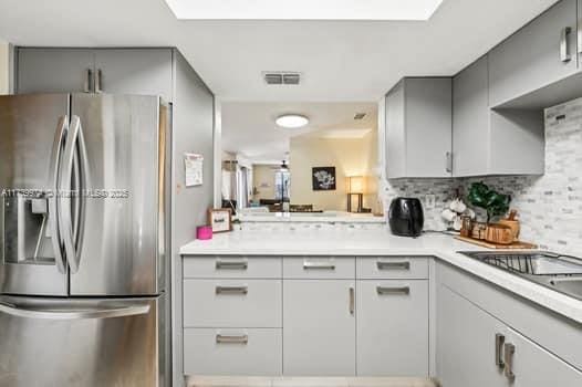 kitchen with a skylight, visible vents, light countertops, backsplash, and stainless steel fridge