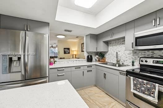 kitchen with stainless steel appliances, gray cabinets, light countertops, backsplash, and a sink