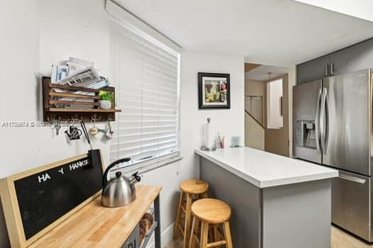 kitchen with a peninsula, a kitchen breakfast bar, light countertops, stainless steel refrigerator with ice dispenser, and gray cabinets