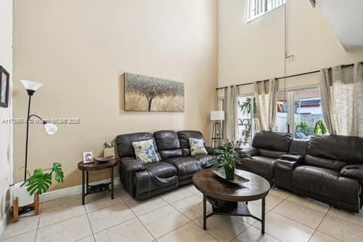 living room with a healthy amount of sunlight, a towering ceiling, baseboards, and light tile patterned flooring