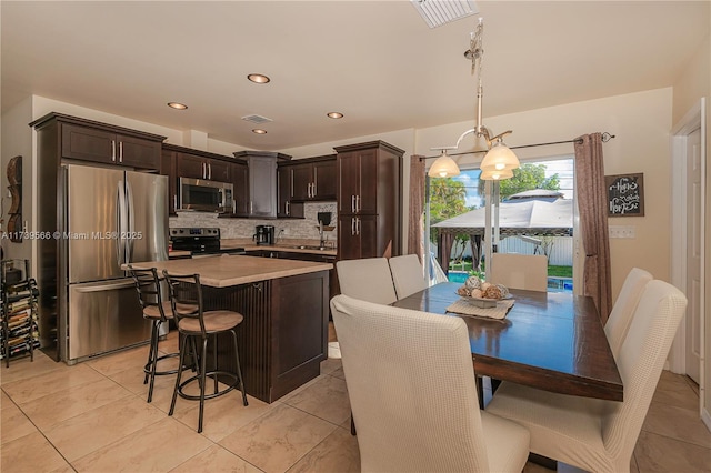 kitchen featuring hanging light fixtures, backsplash, stainless steel appliances, dark brown cabinetry, and a kitchen bar