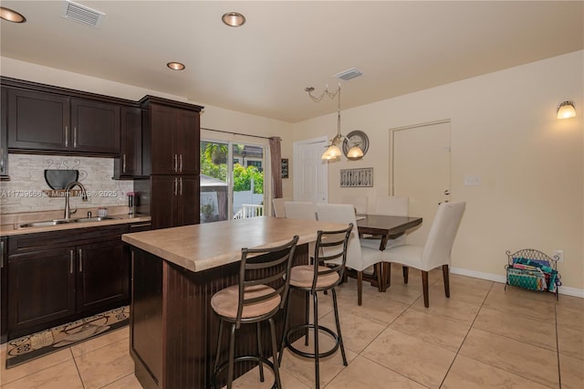 kitchen with a kitchen island, sink, decorative backsplash, hanging light fixtures, and dark brown cabinetry