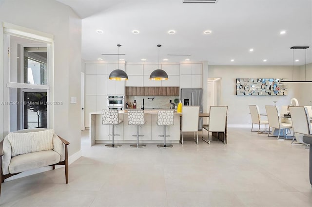 kitchen featuring a breakfast bar, white cabinetry, an island with sink, pendant lighting, and stainless steel appliances