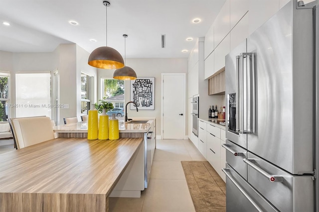 kitchen featuring decorative light fixtures, white cabinets, light tile patterned floors, stainless steel appliances, and a healthy amount of sunlight