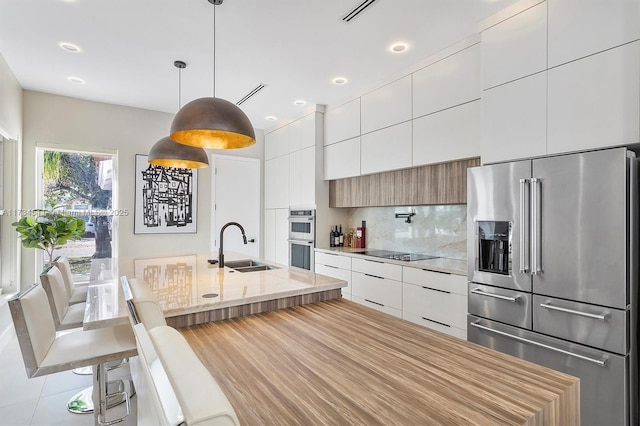 kitchen featuring stainless steel appliances, sink, white cabinets, and decorative light fixtures