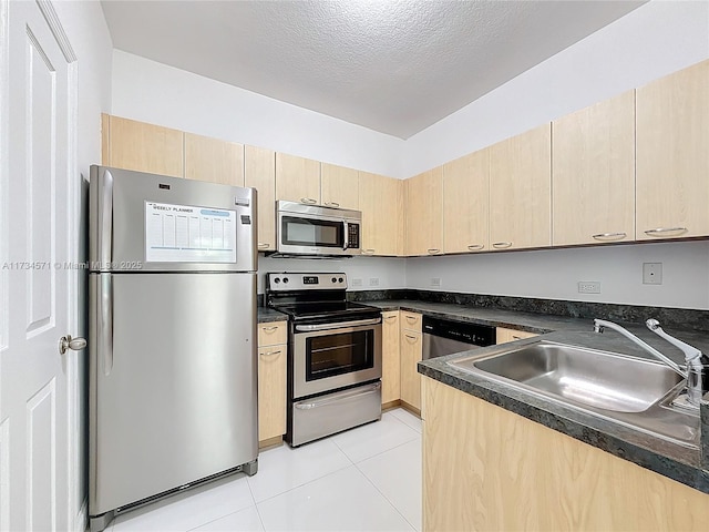 kitchen with light tile patterned flooring, sink, a textured ceiling, light brown cabinets, and appliances with stainless steel finishes