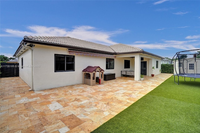 rear view of property with a trampoline and a patio