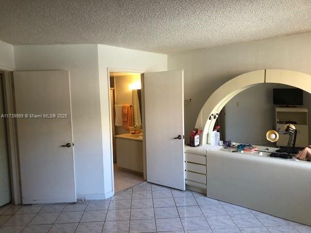 unfurnished bedroom featuring light tile patterned floors, ensuite bath, and a textured ceiling