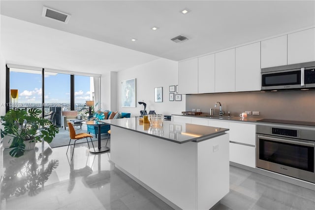 kitchen featuring sink, appliances with stainless steel finishes, a center island, floor to ceiling windows, and white cabinets