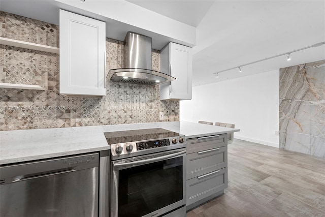 kitchen with tasteful backsplash, white cabinetry, stainless steel appliances, wall chimney range hood, and light wood-type flooring