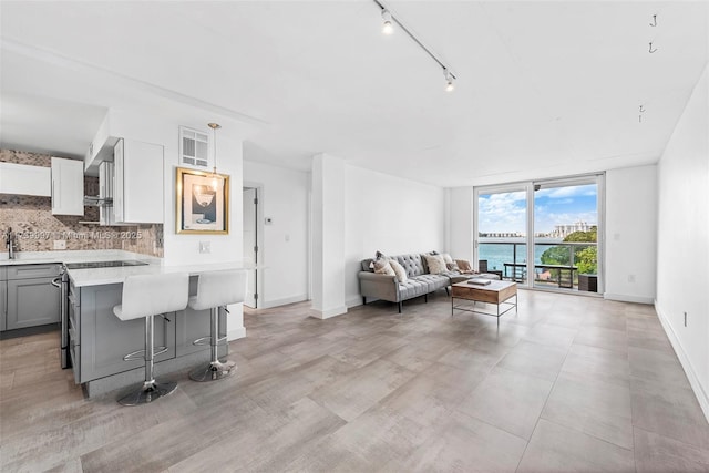 kitchen featuring floor to ceiling windows, gray cabinets, light countertops, backsplash, and a kitchen breakfast bar