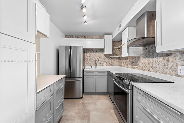 kitchen featuring stainless steel appliances, backsplash, gray cabinetry, a sink, and wall chimney range hood