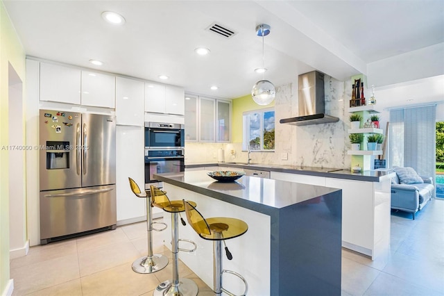 kitchen featuring appliances with stainless steel finishes, white cabinets, a kitchen island, decorative light fixtures, and wall chimney exhaust hood