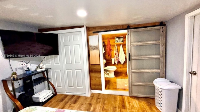 bedroom with connected bathroom, a barn door, and light wood-type flooring