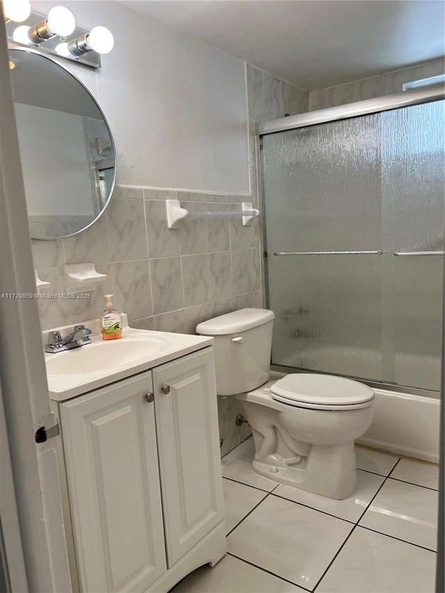 full bathroom featuring bath / shower combo with glass door, vanity, toilet, and tile walls