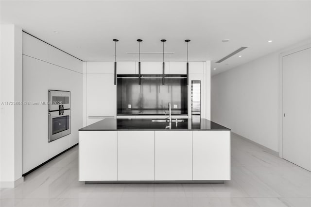 kitchen with a kitchen island with sink, sink, white cabinets, and decorative light fixtures