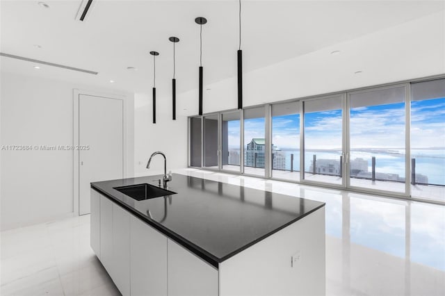 kitchen featuring decorative light fixtures, sink, white cabinets, a wall of windows, and a center island with sink