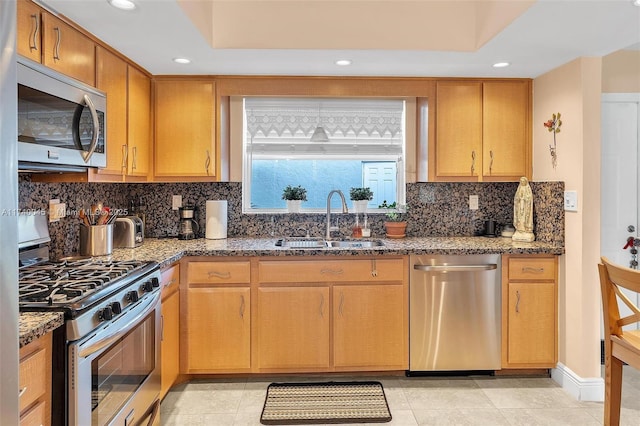 kitchen featuring decorative backsplash, appliances with stainless steel finishes, light stone counters, and a sink