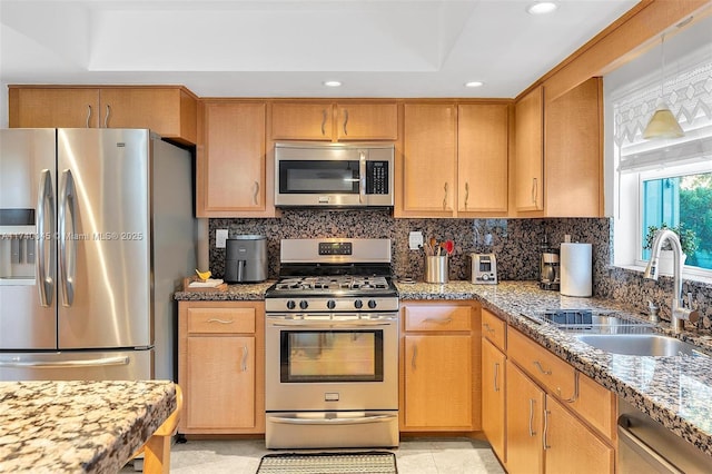 kitchen featuring light stone counters, a sink, appliances with stainless steel finishes, decorative backsplash, and a tray ceiling