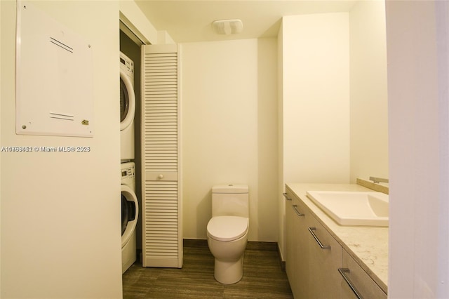 bathroom with stacked washer / dryer, vanity, wood-type flooring, and toilet