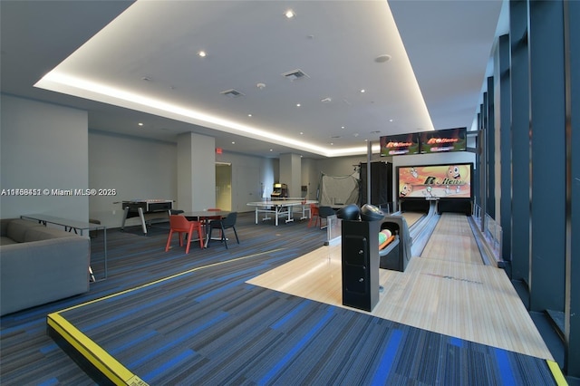 game room with a tray ceiling, carpet floors, and bowling