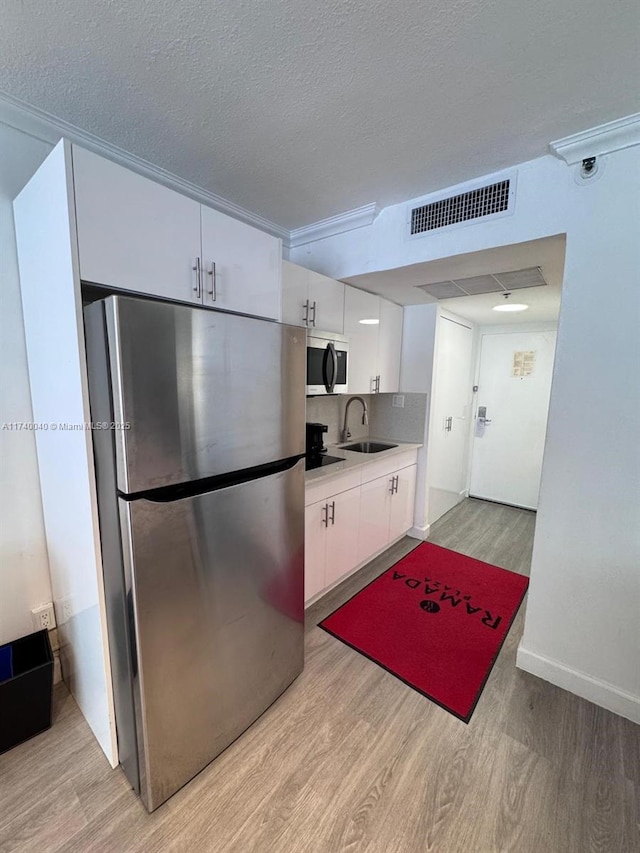 kitchen featuring appliances with stainless steel finishes, white cabinetry, sink, light hardwood / wood-style floors, and a textured ceiling