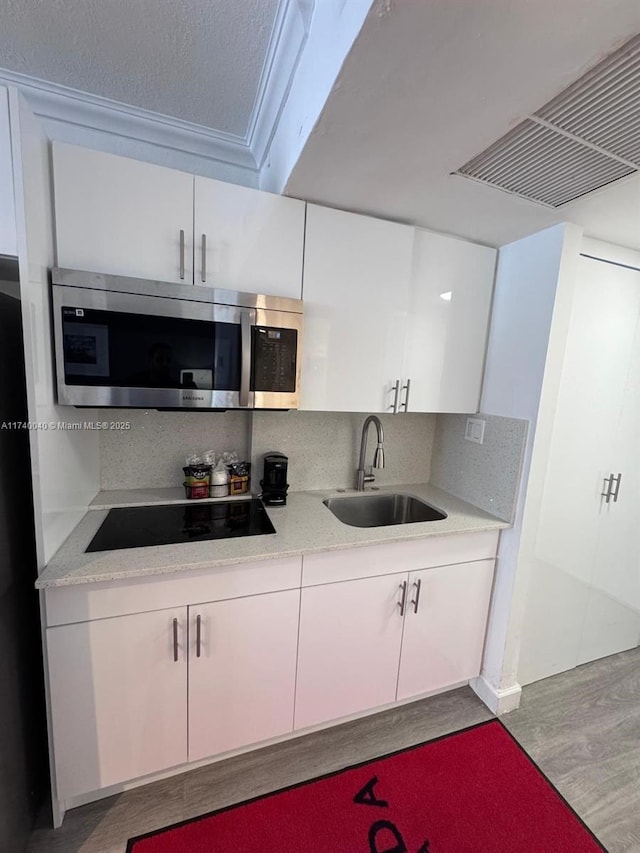 kitchen with sink, backsplash, white cabinets, black electric stovetop, and light hardwood / wood-style floors