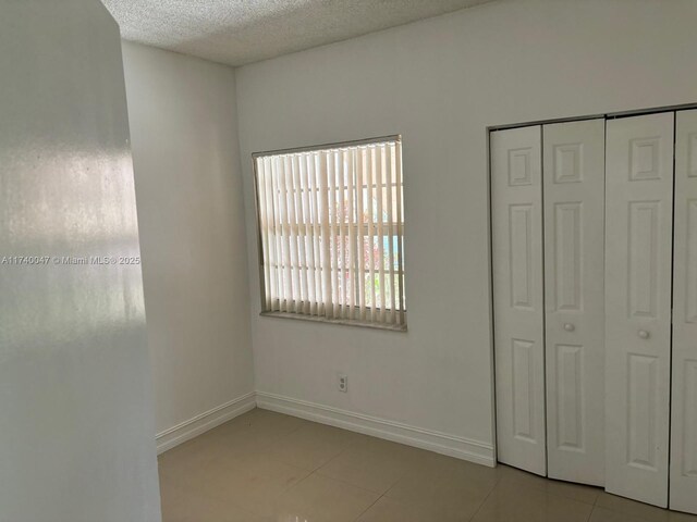 620 Cypress Club Way Unit I13, Deerfield Beach, FL 33064 - unfurnished bedroom featuring a textured ceiling, light tile patterned flooring, a closet, and baseboards