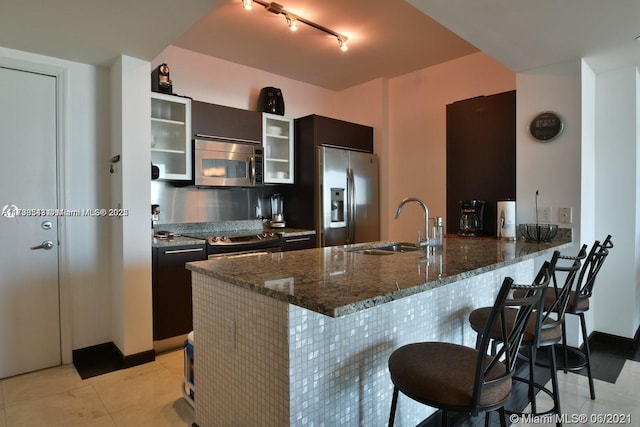 kitchen featuring sink, a breakfast bar, appliances with stainless steel finishes, dark stone countertops, and kitchen peninsula