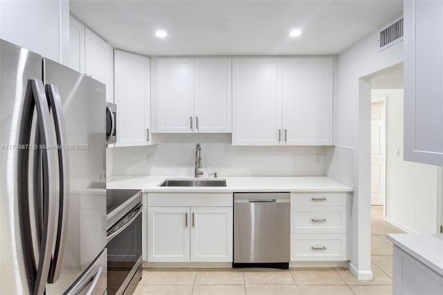 kitchen with sink, white cabinetry, light tile patterned floors, appliances with stainless steel finishes, and decorative backsplash