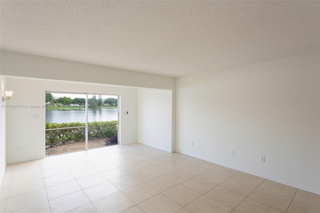 unfurnished room featuring a water view, a textured ceiling, and light tile patterned floors