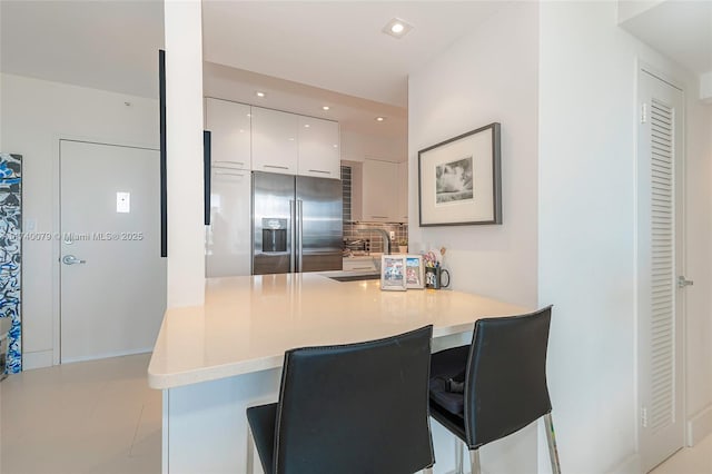 kitchen with high quality fridge, a breakfast bar, sink, white cabinets, and kitchen peninsula