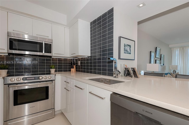 kitchen featuring appliances with stainless steel finishes, tasteful backsplash, white cabinetry, sink, and kitchen peninsula