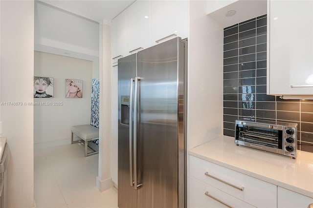 kitchen featuring tasteful backsplash, high quality fridge, and white cabinets