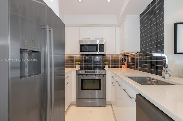 kitchen with sink, white cabinetry, light tile patterned floors, appliances with stainless steel finishes, and decorative backsplash