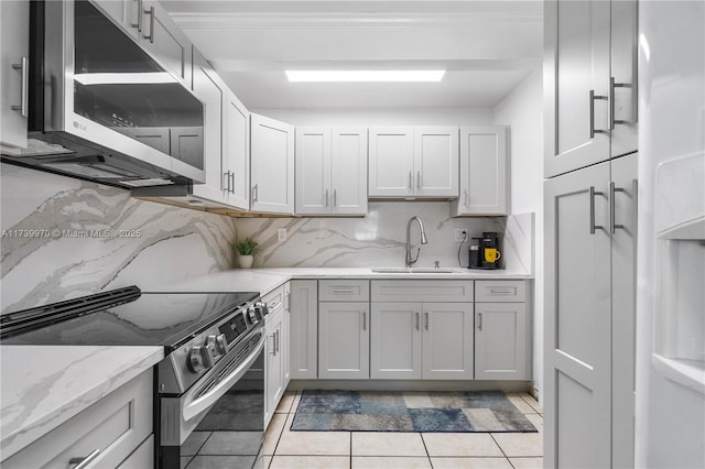 kitchen featuring light tile patterned flooring, sink, light stone counters, stainless steel appliances, and backsplash