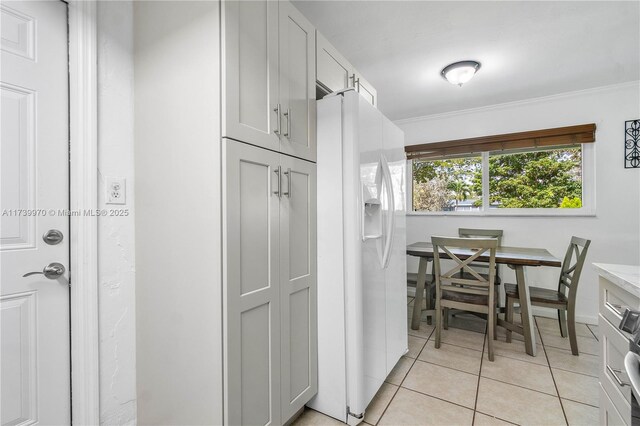 interior space featuring light tile patterned floors, crown molding, white fridge with ice dispenser, and white cabinets