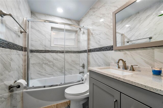 full bathroom with toilet, combined bath / shower with glass door, tile walls, vanity, and backsplash