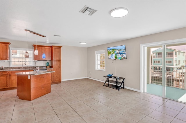 kitchen with hanging light fixtures, light stone countertops, a kitchen island, and a healthy amount of sunlight