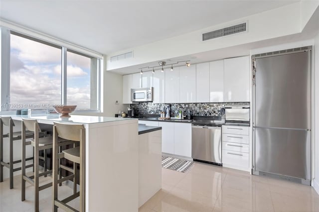 kitchen featuring light tile patterned floors, a breakfast bar area, appliances with stainless steel finishes, white cabinets, and decorative backsplash