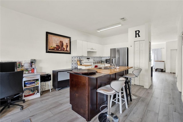 kitchen featuring white electric stove, white cabinetry, an island with sink, sink, and stainless steel refrigerator with ice dispenser