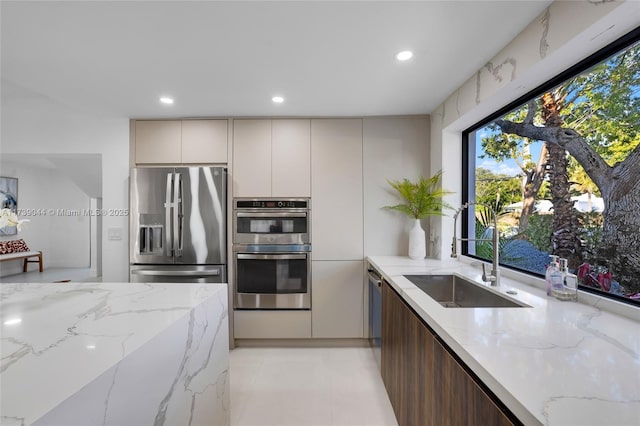 kitchen featuring stainless steel appliances, recessed lighting, a sink, and light stone counters