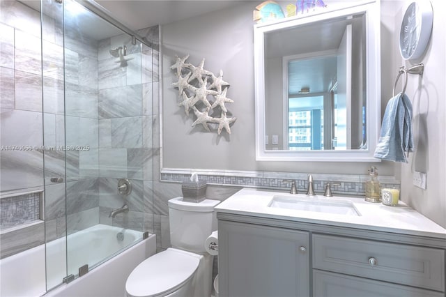 bathroom with tile walls, combined bath / shower with glass door, vanity, and toilet